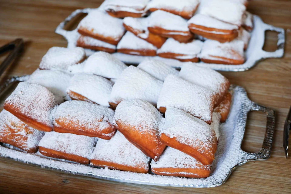 Trays of freshly made beignets dusted with powdered sugar on a wooden table.
