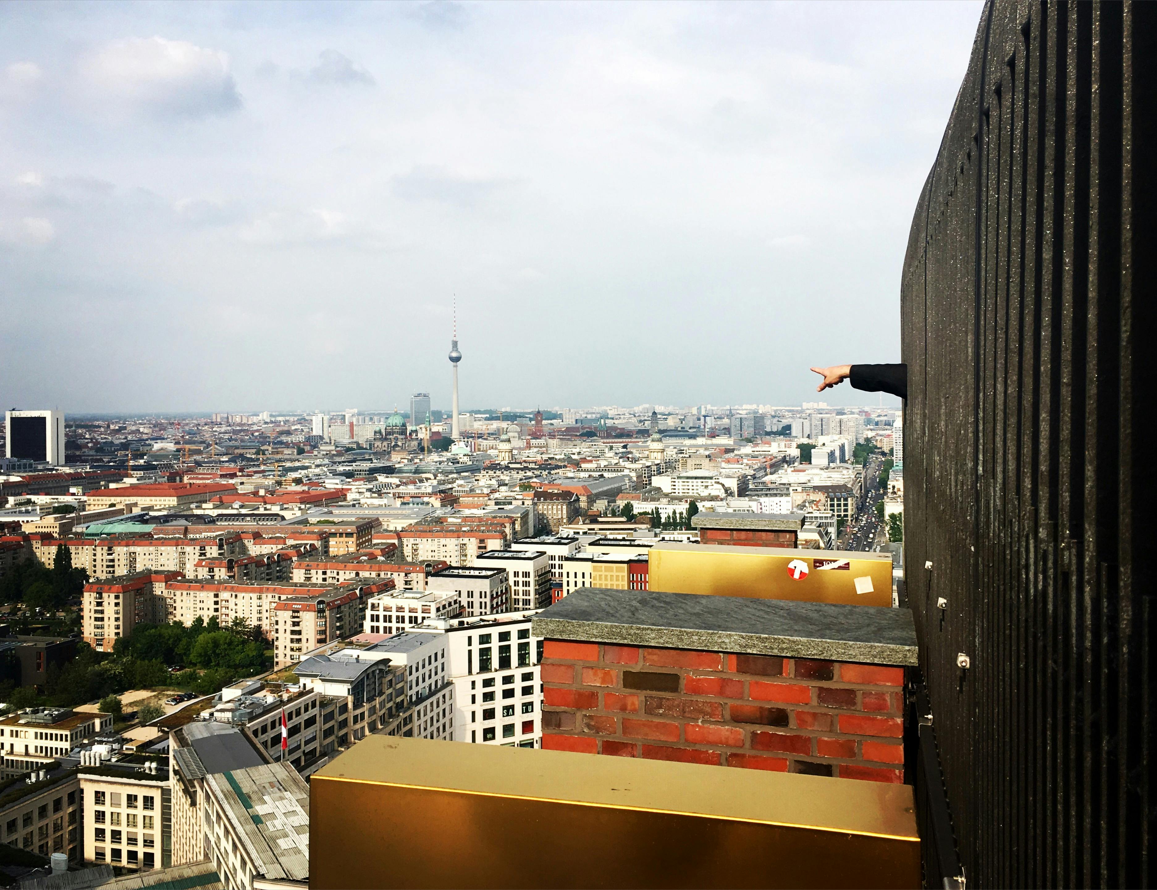 Stadsgezicht met de Fernsehturm (TV-toren) in de verte. Een persoon wijst in de richting van de stad.