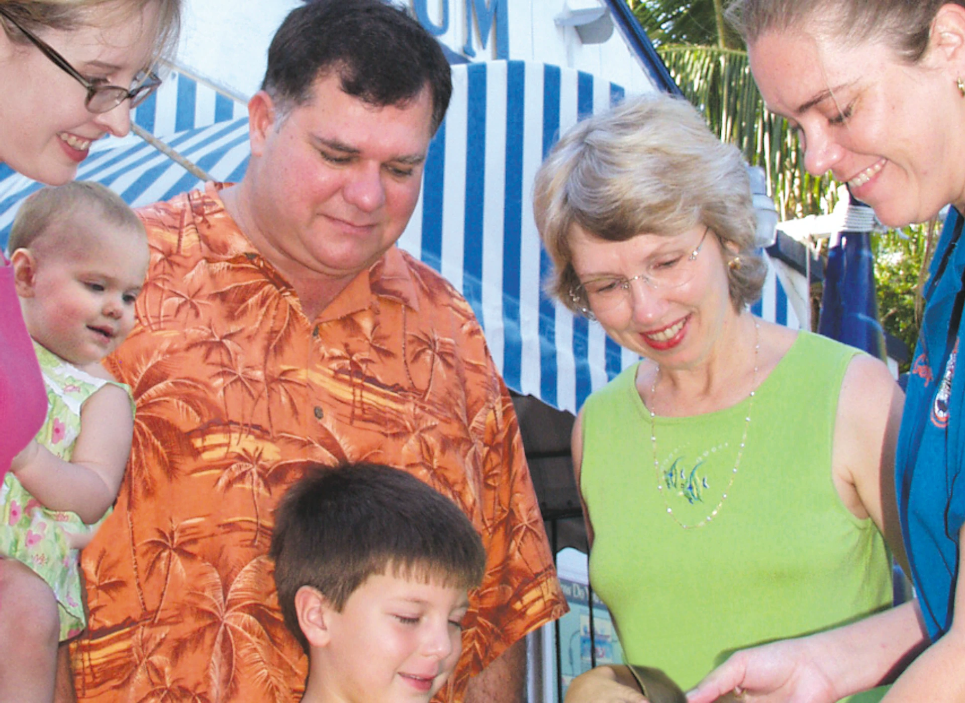 A group of people, including children, admire a small shark held by an aquarium staff outside the Key West Aquarium.