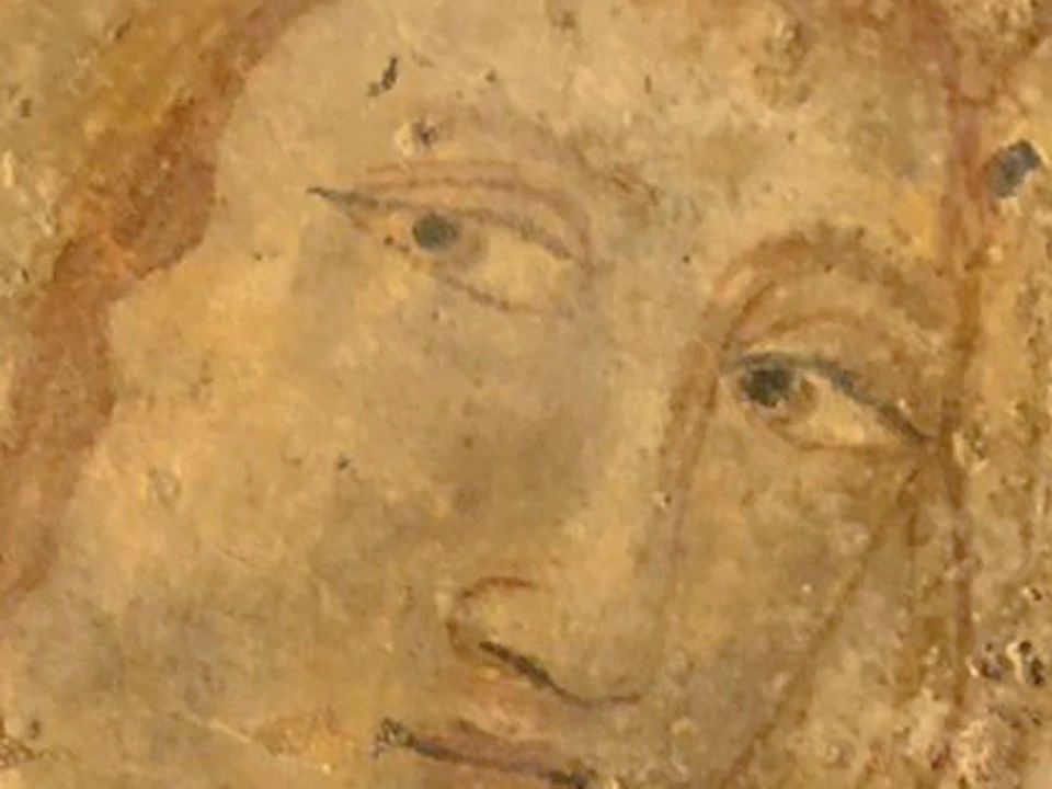 An ancient fresco depicting a serene figure with an illuminated halo, slightly worn and set against a textured, weathered background.
