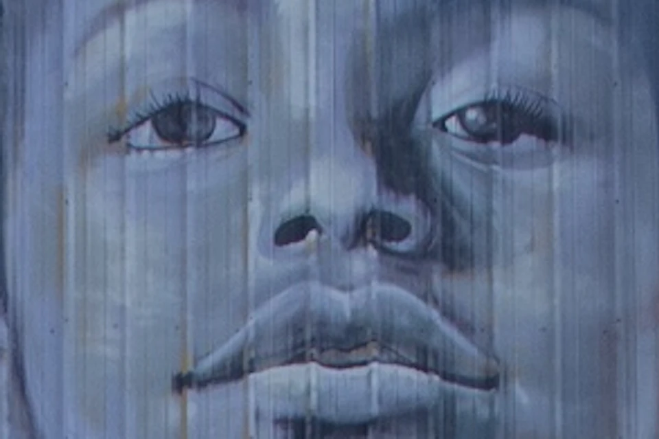 A group of four cyclists stand near their bikes, observing a large mural of a person painted on a yellow building.