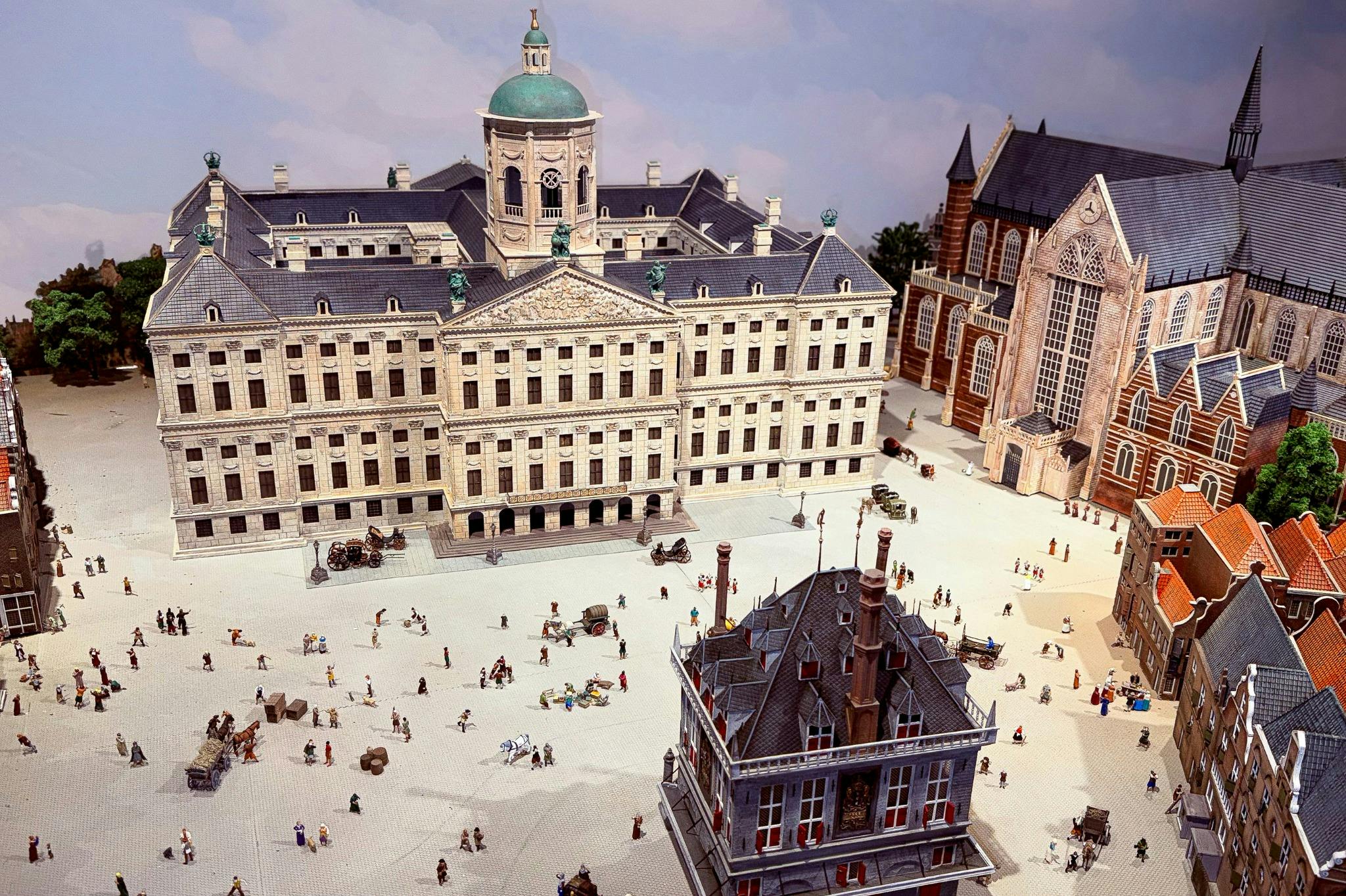 En detaljerad modell av ett historiskt europeiskt torg med byggnader, små figurer, hästdragna vagnar och träd.