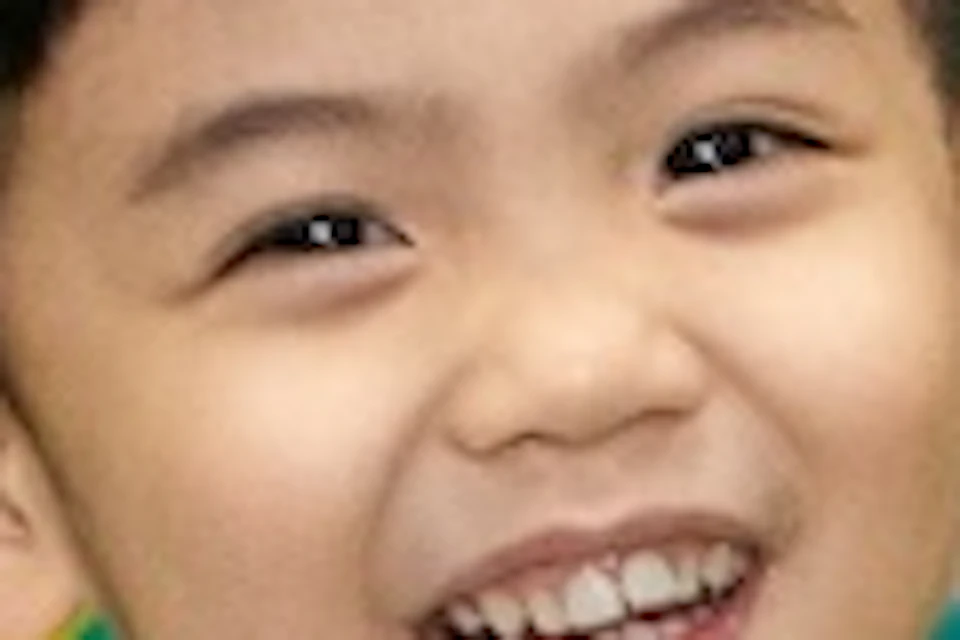 A child smiling and playing in a colorful ball pit next to a green slide in an indoor play area.