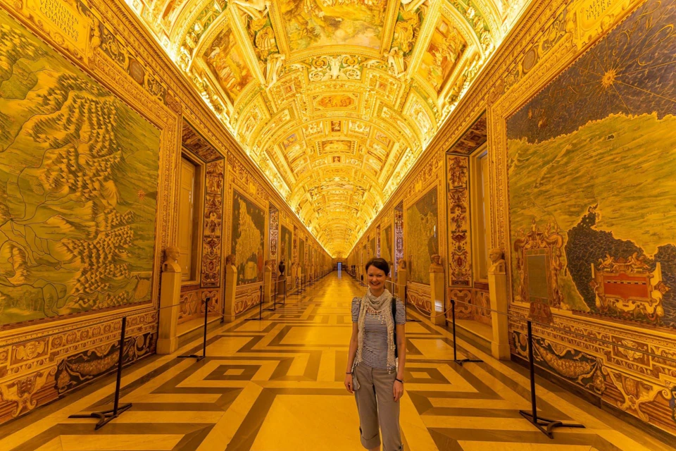 A person stands in a richly decorated, golden-lit corridor with ornate ceilings and detailed wall murals.