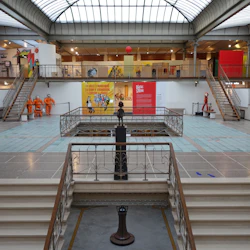 Ett stort atrium med trappor leder till utställningar, färgglada utställningar och skyltdockor i orange kostymer. Taket är tillverkat av glasrutor.