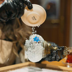 Deltagaren häller små vita stenar på en mosaiklampa som tillverkas.