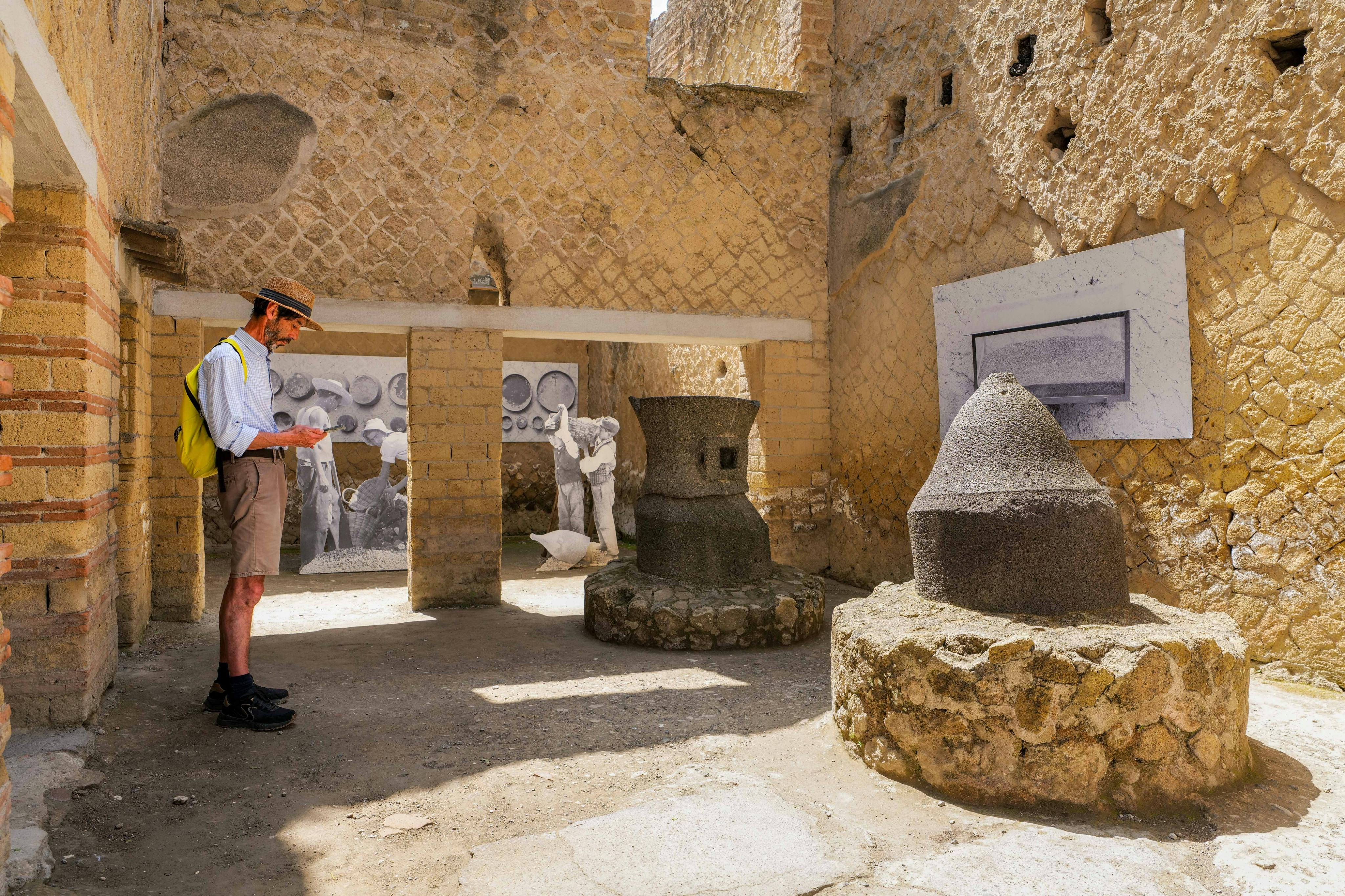 帽子とショートパンツを着た人が、壁に石の工芸品と歴史的な壁画が描かれた古代遺跡を調べています。