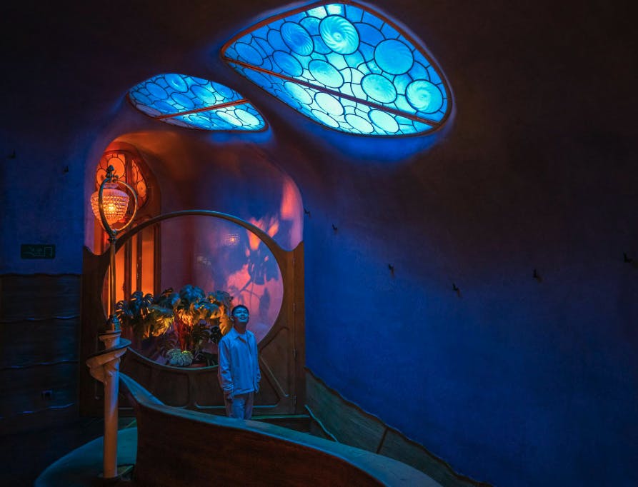 A person stands in a room with organic architecture, blue-lit ceiling windows, and warm decorative lighting.