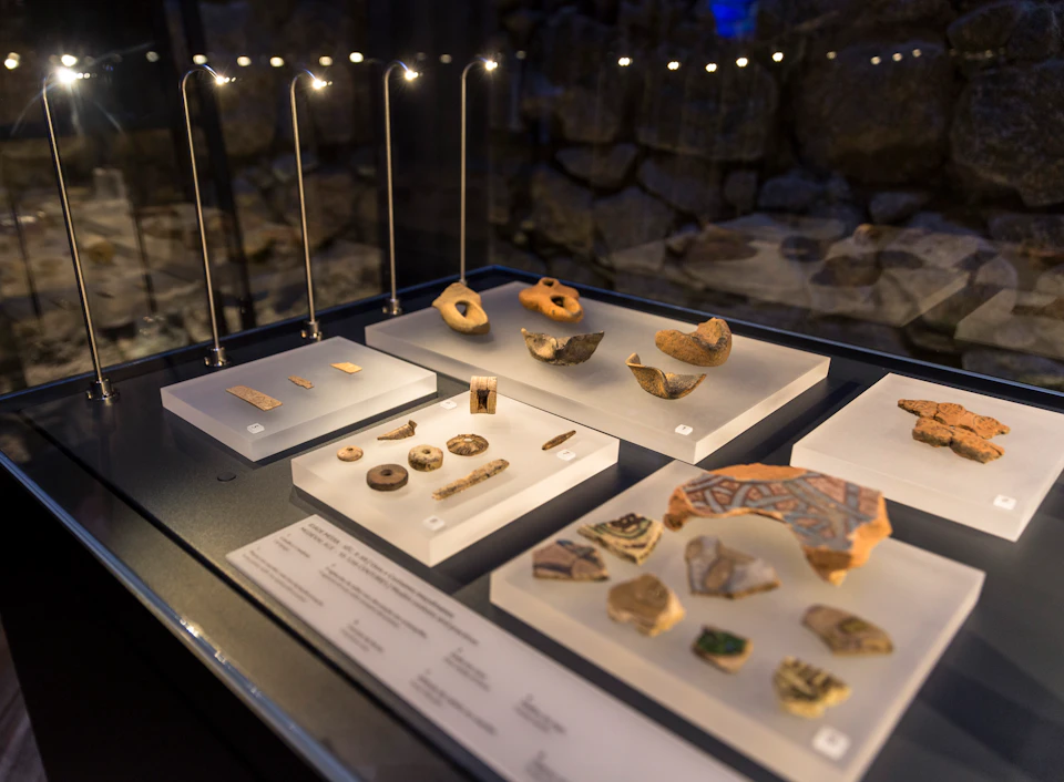 Display case with archaeological artifacts, including pottery shards, beads, and tools, illuminated by overhead lights.