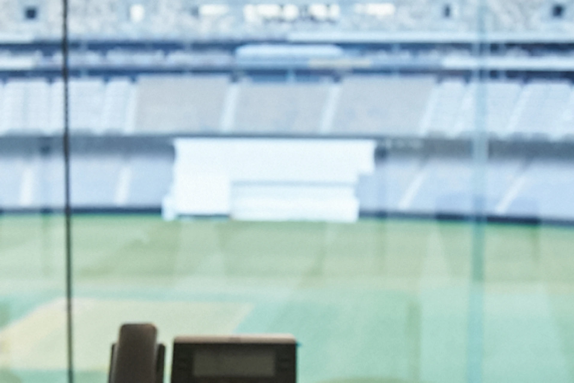 A smiling boy sits in a chair in a stadium press box, with a view of the empty field behind him.