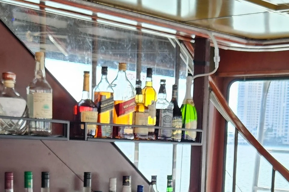 A bartender in a red shirt is pouring a drink for a customer at a bar with bottles in the background, on a boat.