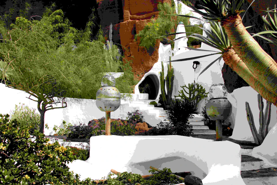 A white, dome-shaped building with steps, surrounded by lush green vegetation and unique sculptures.