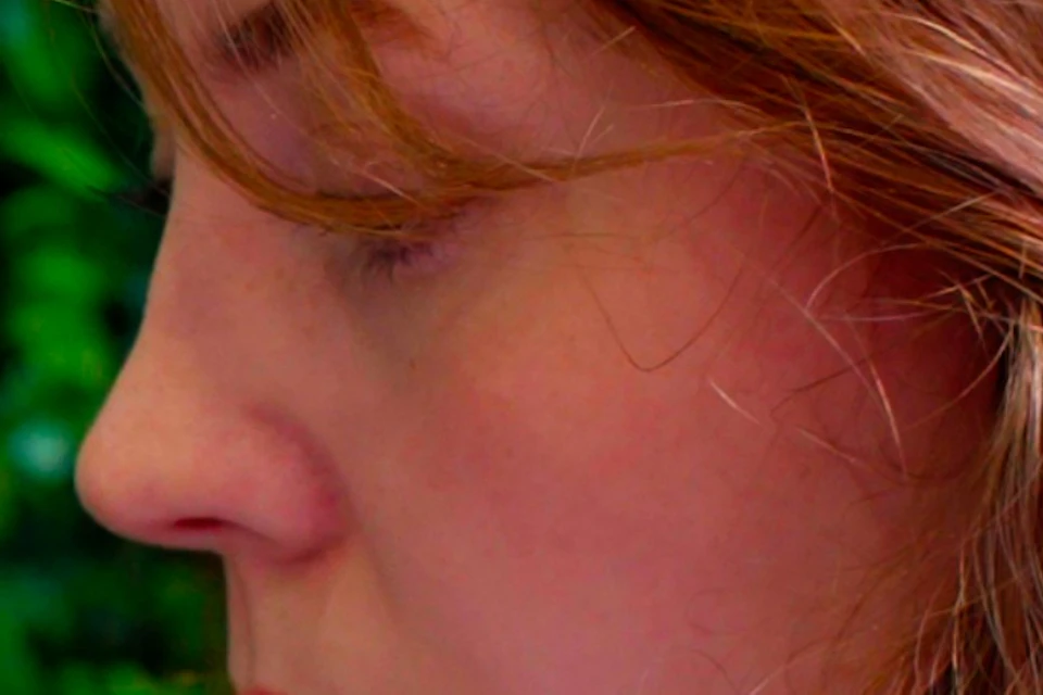 Person with long, red hair works with a metal tool alongside a hammer against a backdrop of lush green plants.