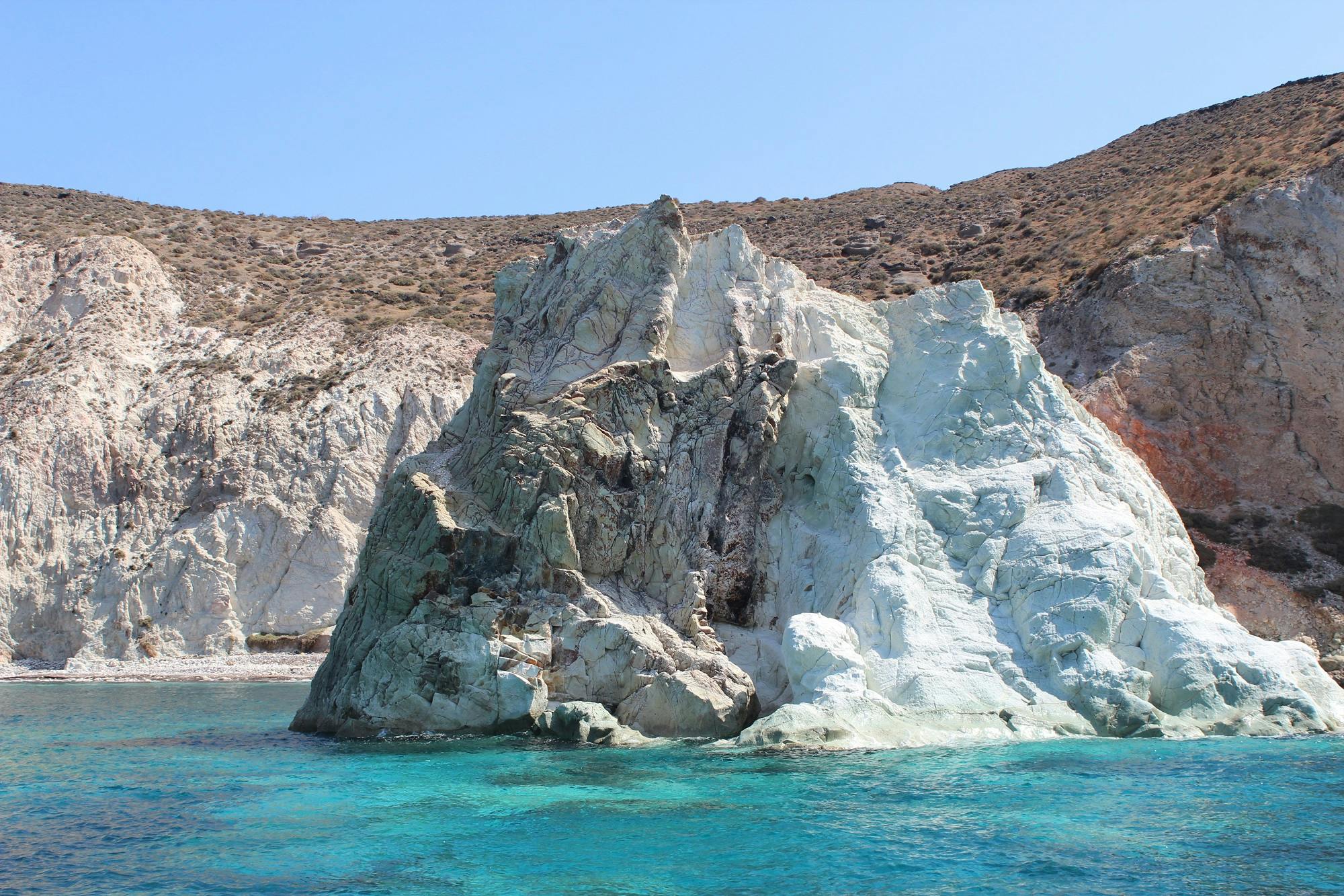 청록색 물로 둘러싸인 맑고 푸른 하늘을 배경으로 커다란 흰색과 회색의 돌이 형성된 바위 해안선.