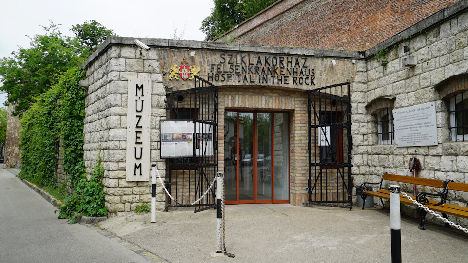 Entrance to “Hospital in the Rock” museum with double gates, informational boards, and signage in multiple languages.