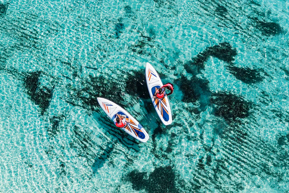 Two people paddleboarding on clear turquoise water with visible dark patches below the surface.
