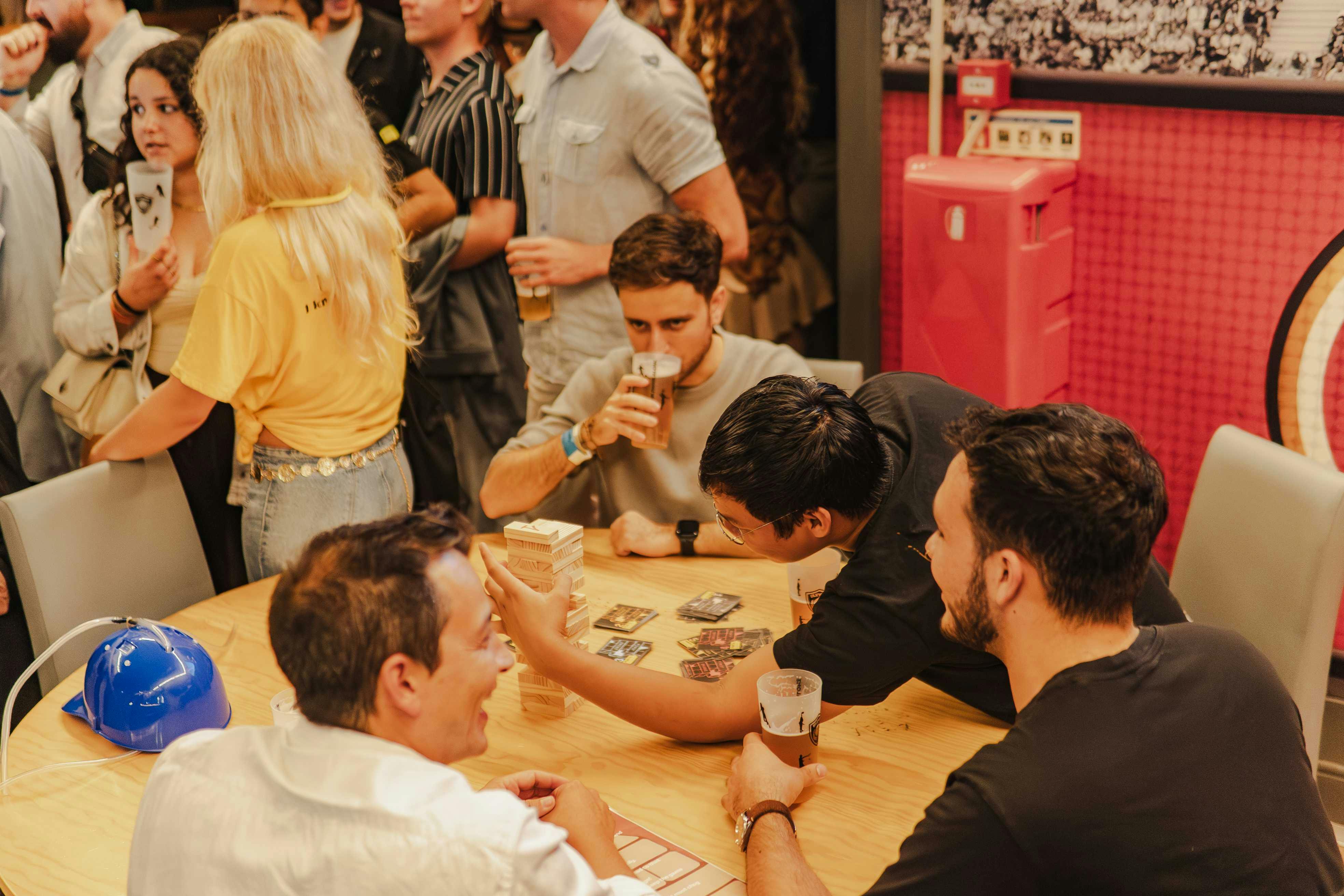 Mensen verzamelden zich binnen, sommigen speelden spelletjes aan een tafel terwijl anderen praatten en drankjes vasthielden, waardoor een levendige sfeer ontstond.