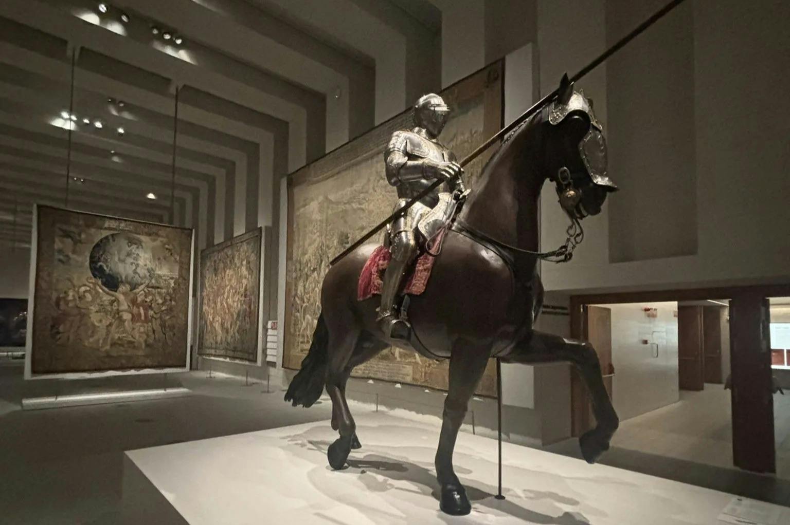 馬に乗ったフルアーマーの騎士が展示されている博物館で、背景にはタペストリーが展示されています。