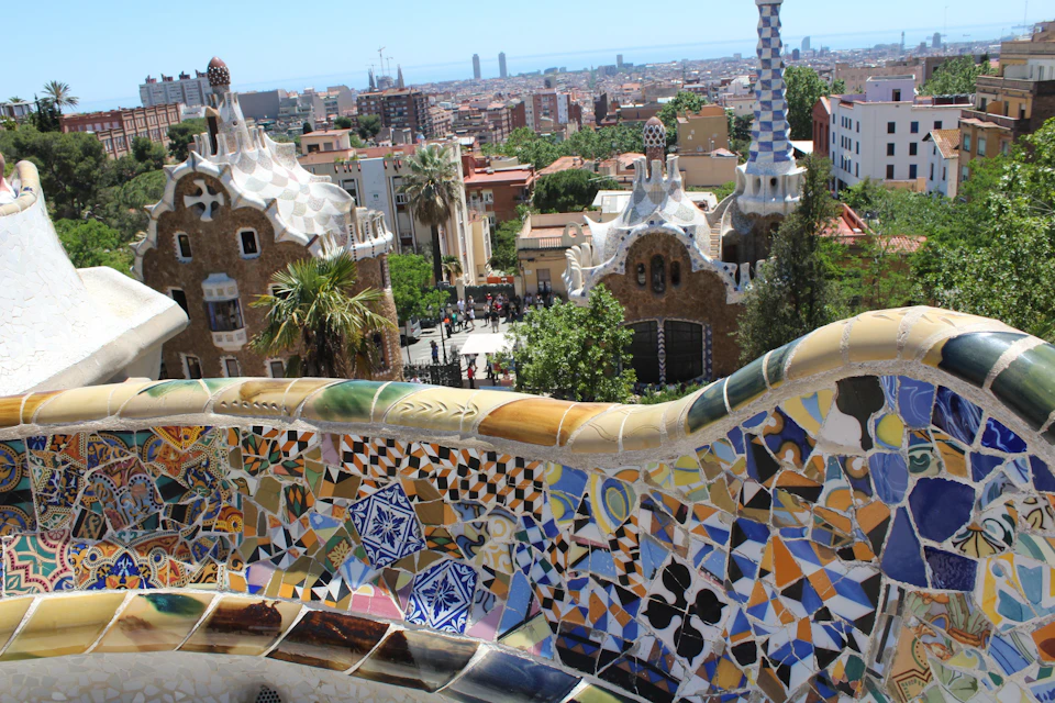Mosaic-tiled terrace overlooking Gaudí's architecture and cityscape at Park Güell, Barcelona, with distant city buildings.