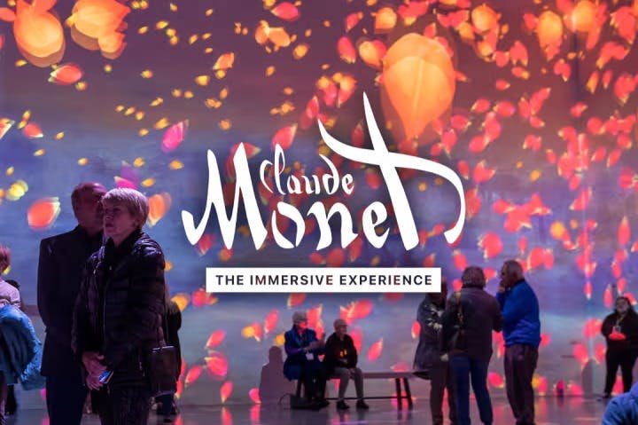 Folk står og sidder i et rum med farverige, animerede projektioner af Claude Monets kunstværk og teksten "Claude Monet: The Immersive Experience."