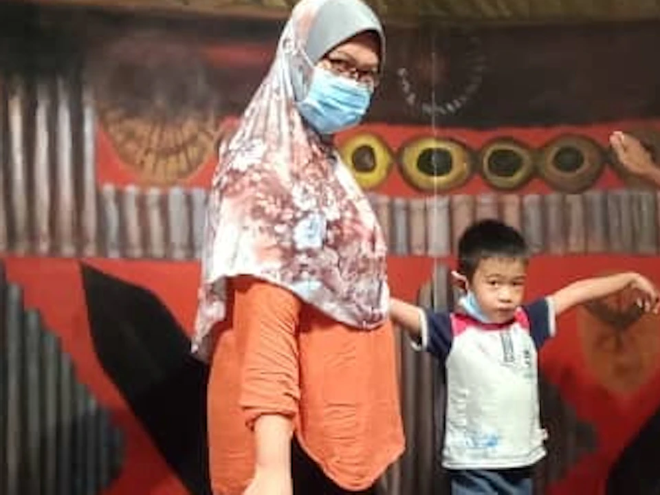 A family posing on a wooden floor with a cultural backdrop featuring traditional dancers and bamboo poles.