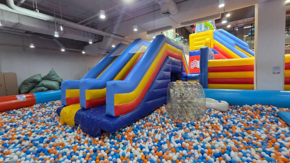 Indoor inflatable slide with blue, yellow, and red colors, surrounded by a ball pit filled with multicolored balls.