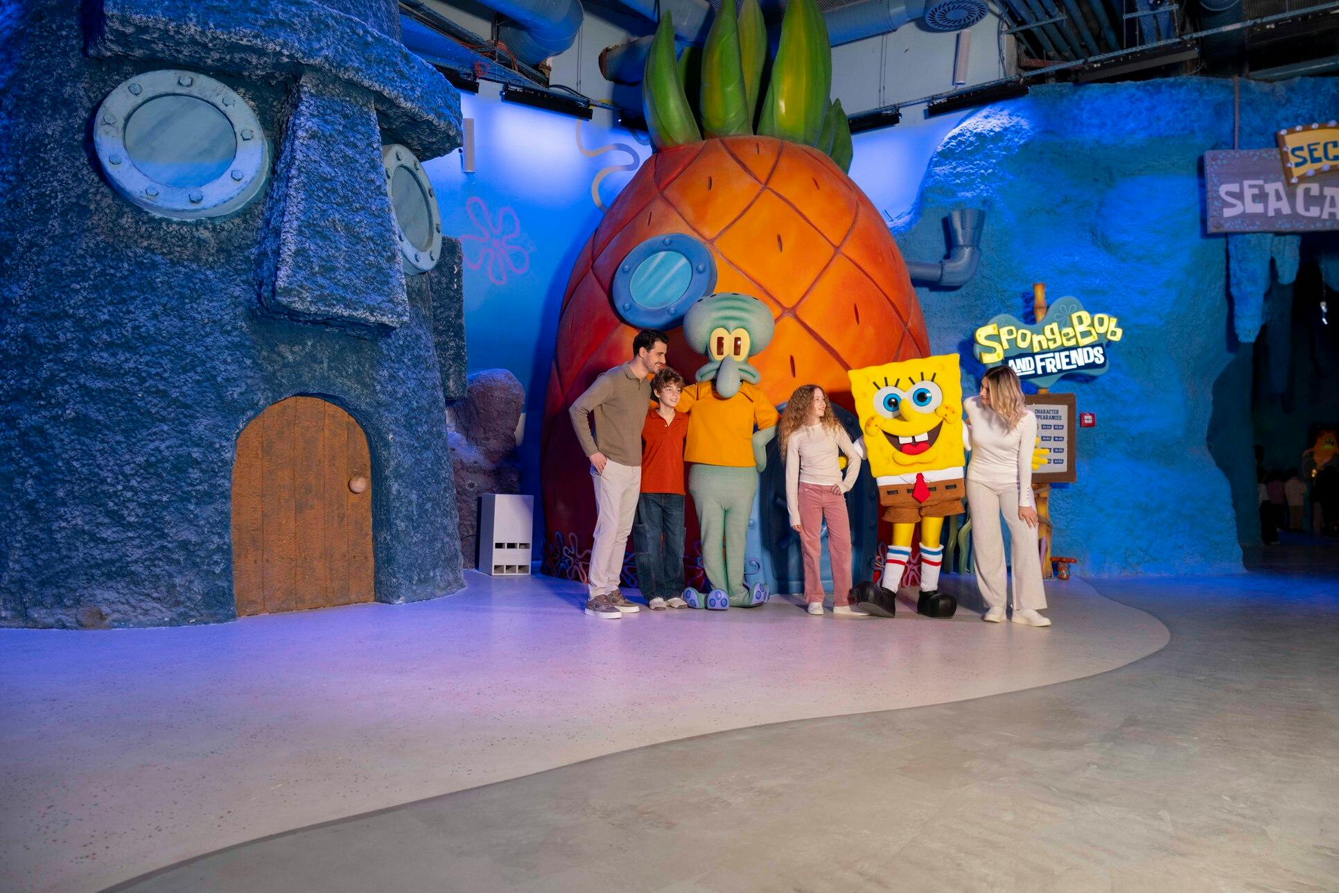 Groep mensen die poseren met de personages SpongeBob SquarePants en Squidward in een thema-omgeving met iconische onderwaterhuizen.