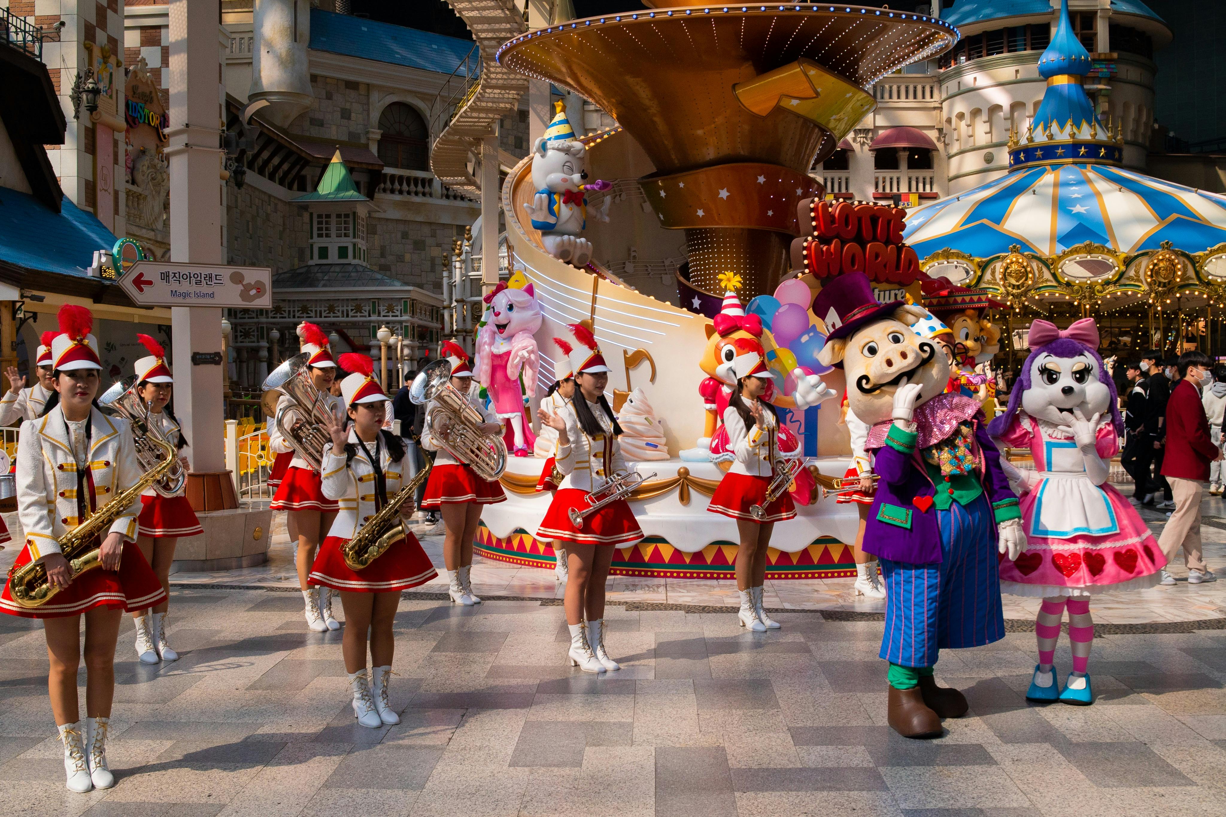 お祝いのユニフォームを着たマーチングバンドは、動物のマスコットと風船を備えたカラフルなパレードフロートの横で真鍮製の楽器を演奏します。