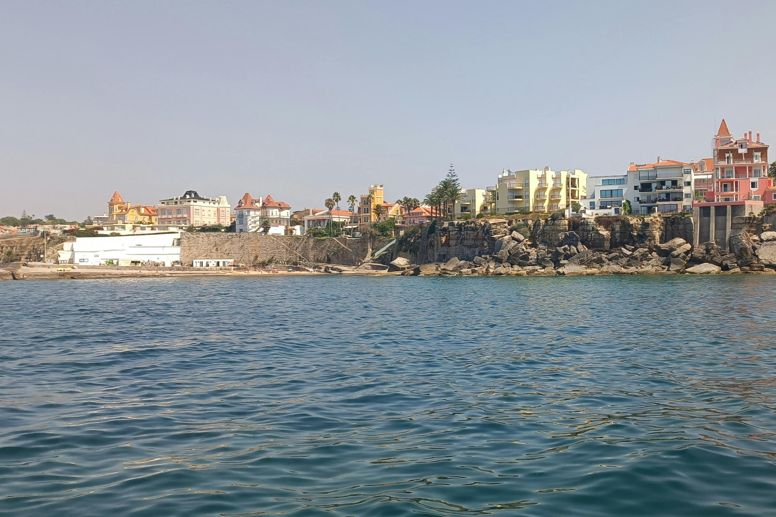 澄んだ空の下、水上から見える岩だらけの海岸沿いの町。