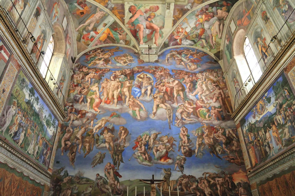 A detailed fresco depicting numerous figures in dynamic poses, covering the wall of an ornate, vaulted ceiling room.