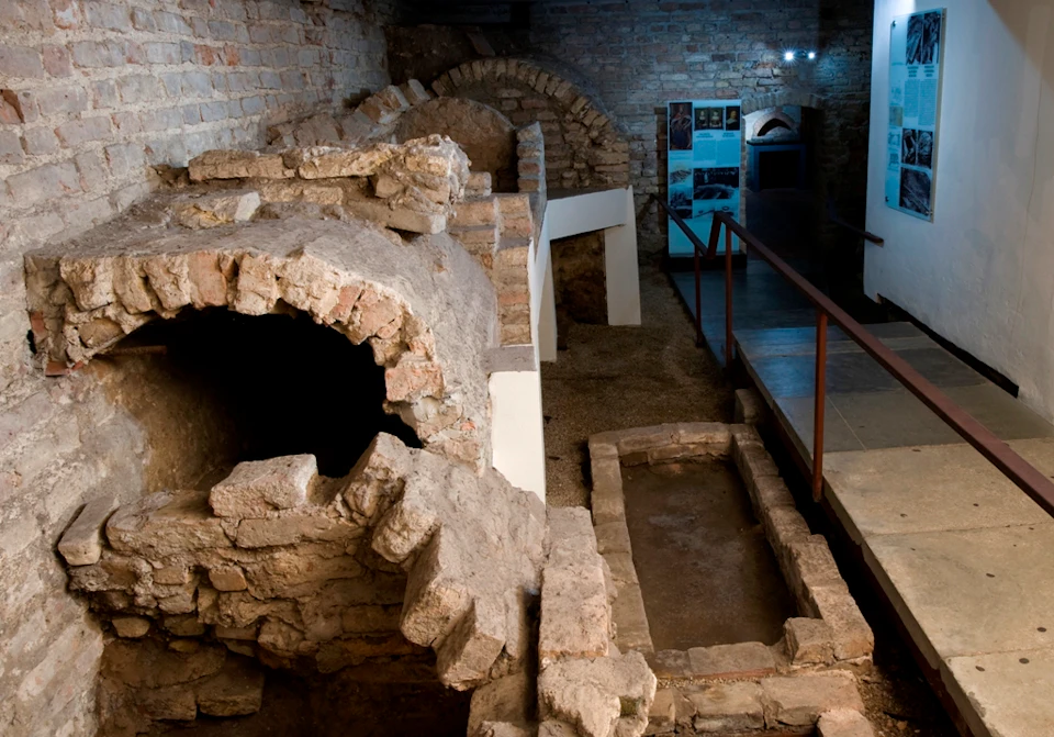 Ancient underground ruins with stone arches and pathways, informational display boards, and ambient lighting.