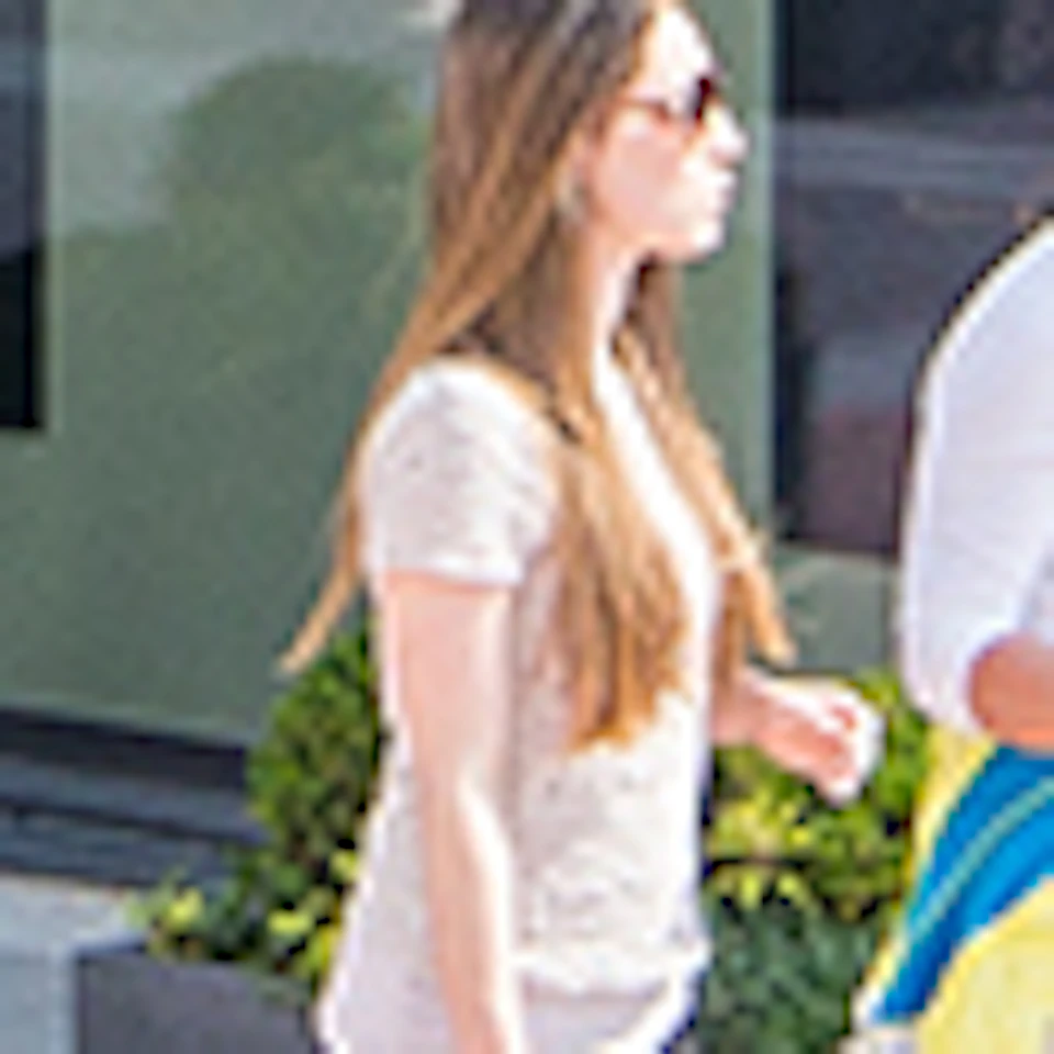 People walking and shopping on a sunny day in a pedestrian area with pastel-colored buildings, storefronts, and decorative plants.