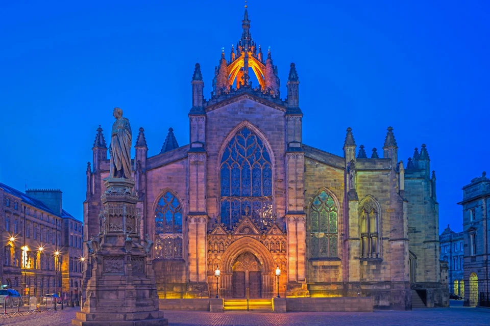 A historic church facade illuminated at night, with a statue in the foreground under a deep blue sky.