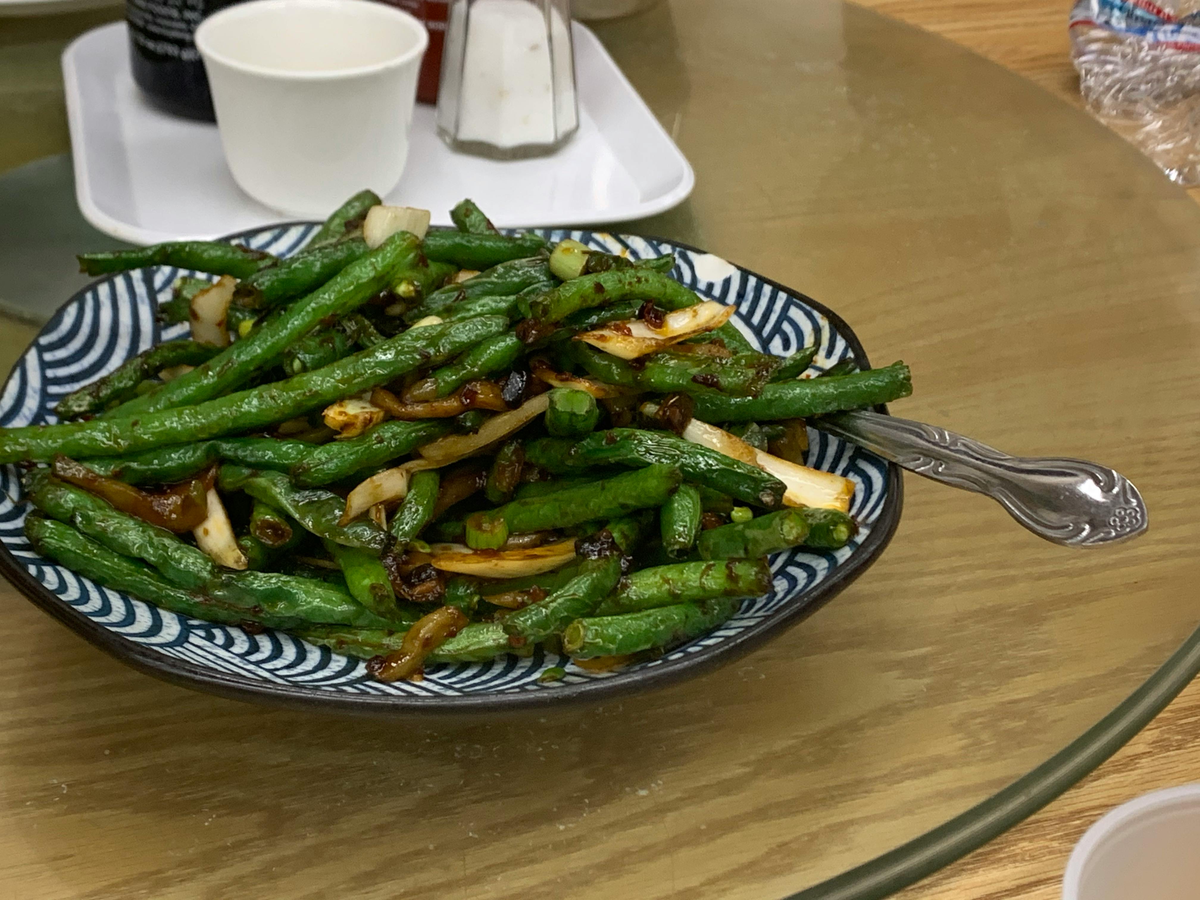 Een bord roergebakken sperziebonen en gesneden knoflook geserveerd op een blauw-wit gedessineerde schaal, met een vork ernaast.