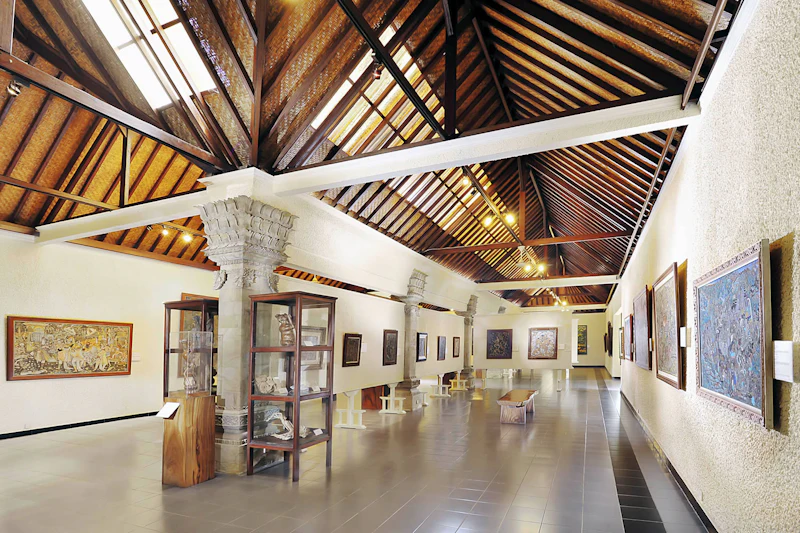Interior of a museum gallery with high wooden ceilings, bright lighting, display cases, and framed art on the walls.
