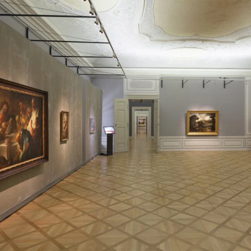 Rymligt konstgalleri med trägolv, inramade målningar på väggar, en dekorativ spis och en hall med mer konstverk synliga.