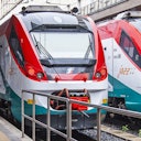 Front view of two modern trains with red and white livery parked side by side on tracks, partially covered by a platform railing.