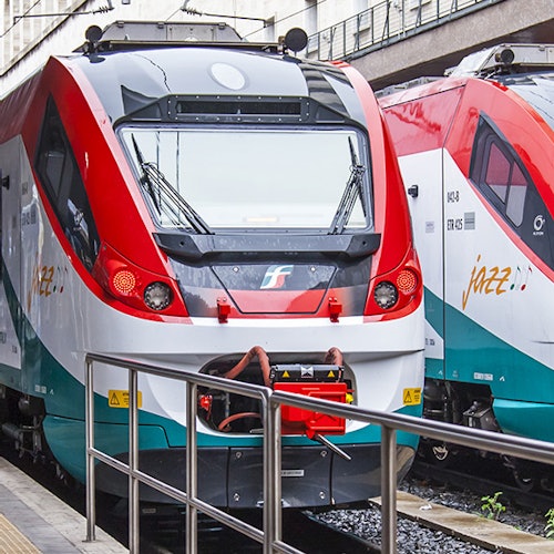 Front view of two modern trains with red and white livery parked side by side on tracks, partially covered by a platform railing.