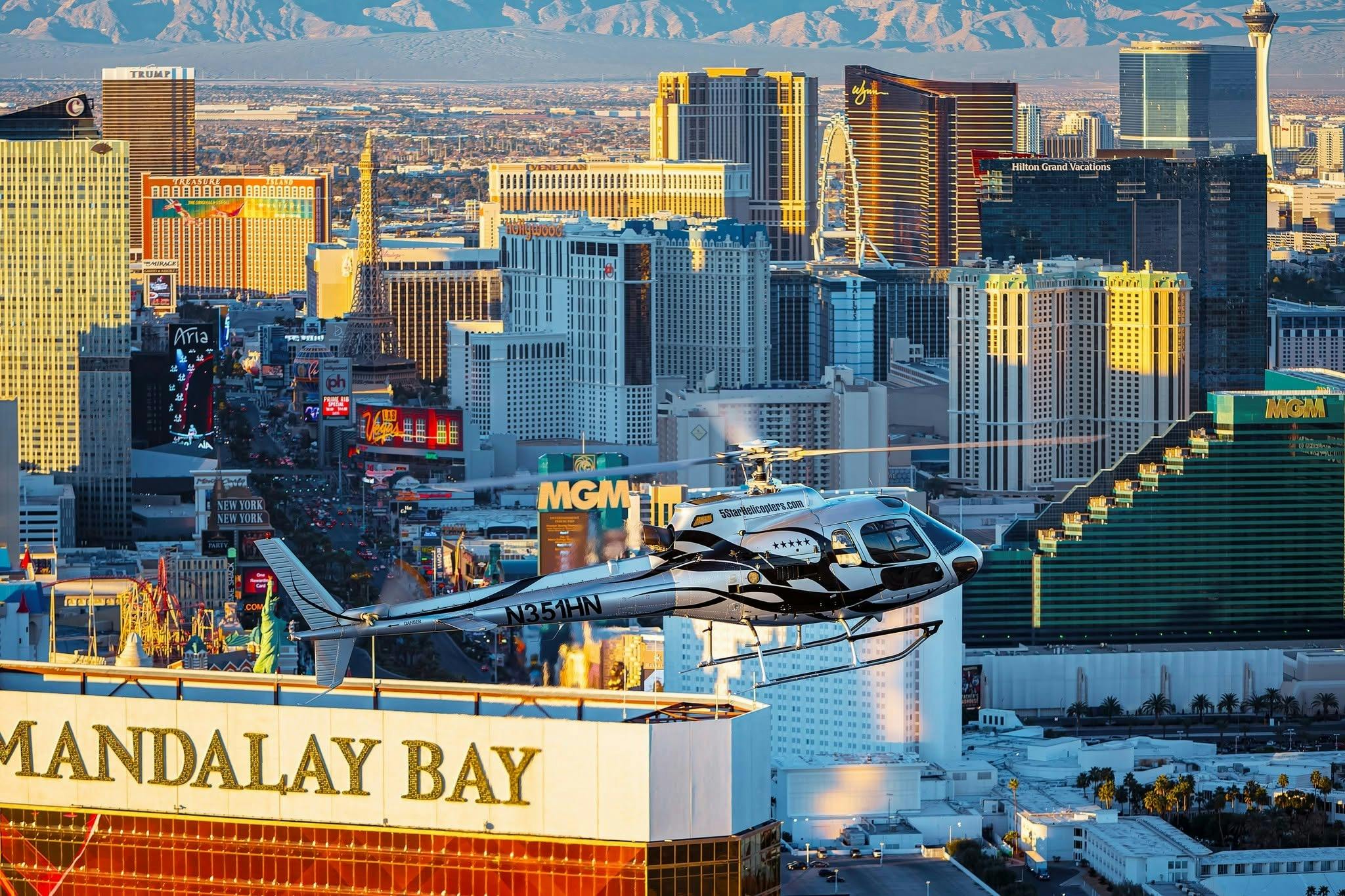 A helicopter flying over Las Vegas with the skyline, including hotels and the High Roller, visible in the background.