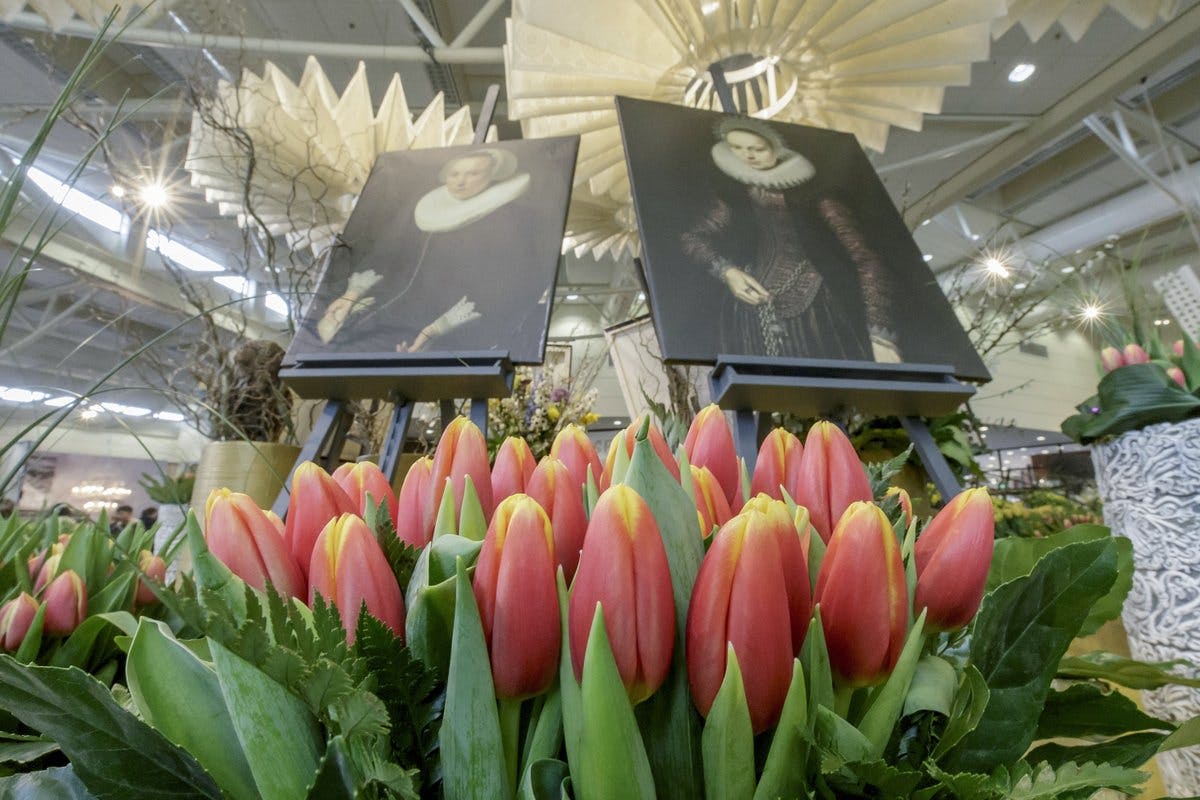 Red and yellow tulips in the foreground with two framed paintings of people in historical attire on easels behind them.