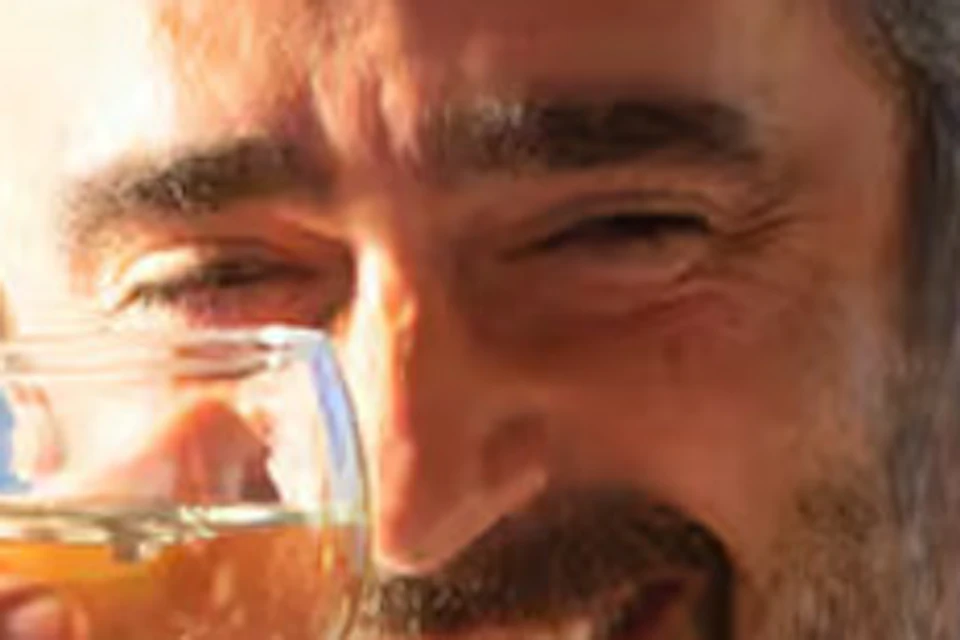 A man and a woman clinking glasses of wine, smiling, seated outdoors with a blurred urban background.