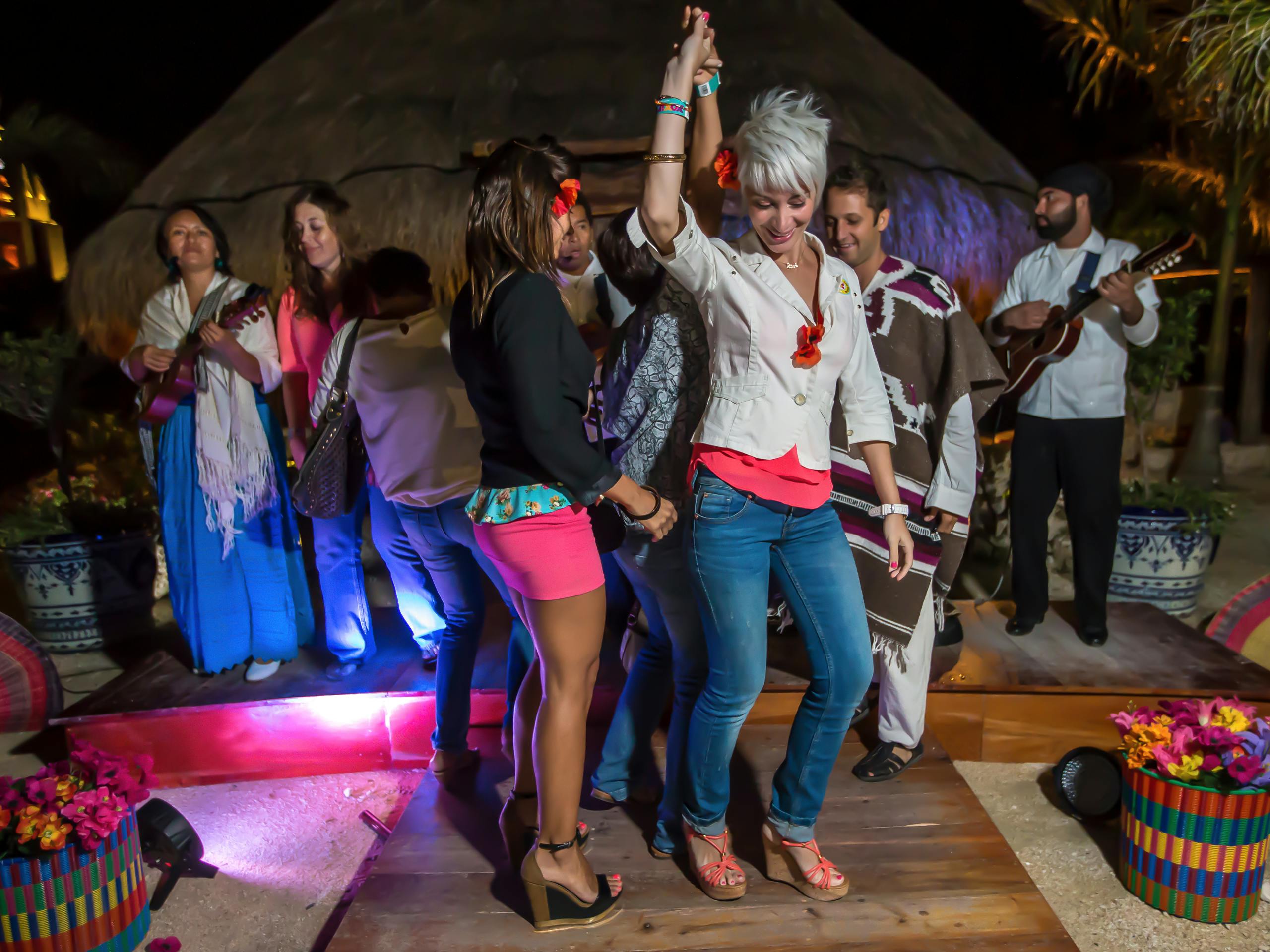 Οι άνθρωποι χορεύουν σε μια σκηνή το βράδυ με έναν κιθαρίστα στο παρασκήνιο. Μια γυναίκα με άσπρα μαλλιά σηκώνει το χέρι της.