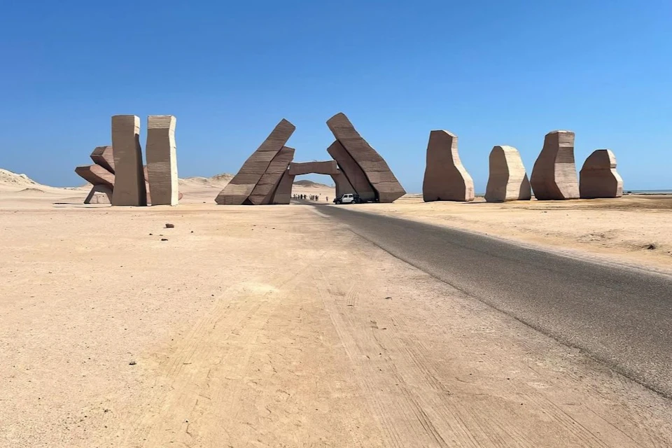 A paved road passing through tall, abstract stone formations in a desert landscape under a clear blue sky.