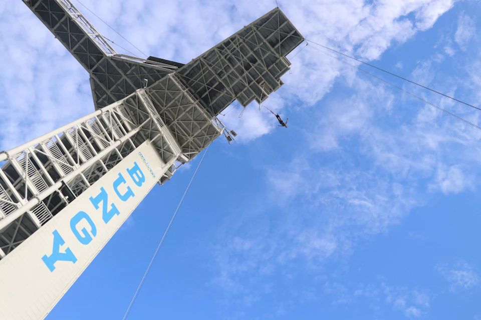 A person bungee jumping from a tall structure under a blue sky with some clouds, seen at a dramatic angle.