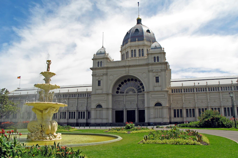 An ornate, domed building with arches and decorative windows, surrounded by green lawns and a fountain in the foreground.