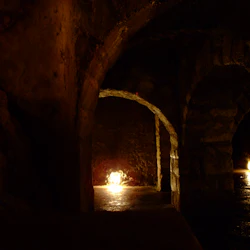 Svagt upplysta stenvalv med små lampor som belyser passagen och grova, strukturerade väggar.