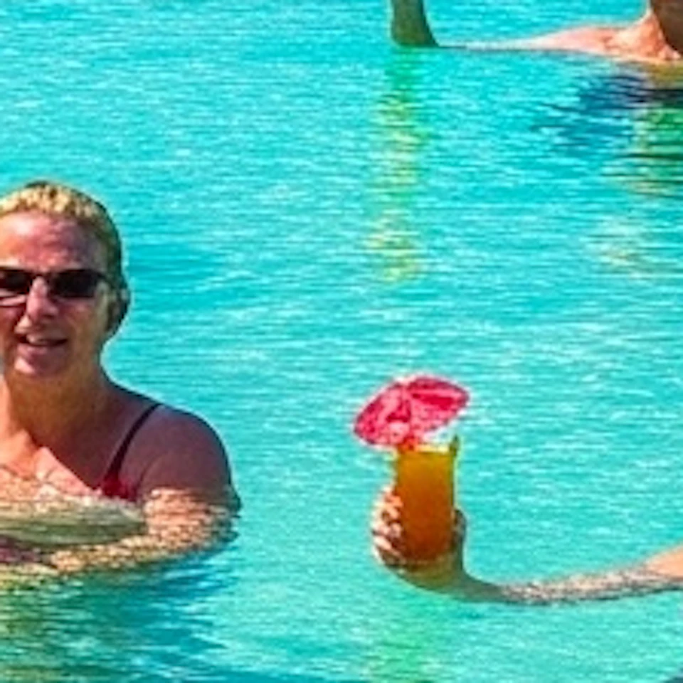 A tropical beach scene with people in clear turquoise water holding drinks, jet skis, and a ship labeled 'Bimini' in the background.