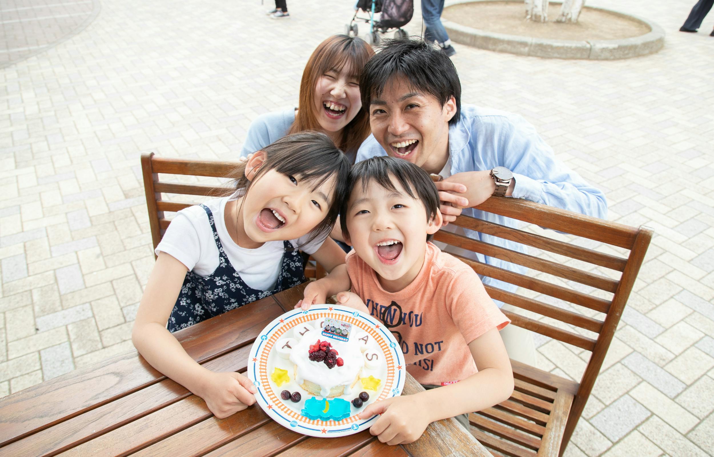 四个人围着桌子微笑，桌上摆放着装饰好的食物。 室外区域似乎有座位。