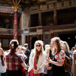 En grupp människor samlades inomhus, några med hörlurar, med en utsmyckad, historisk bakgrund med pelare och balkonger.