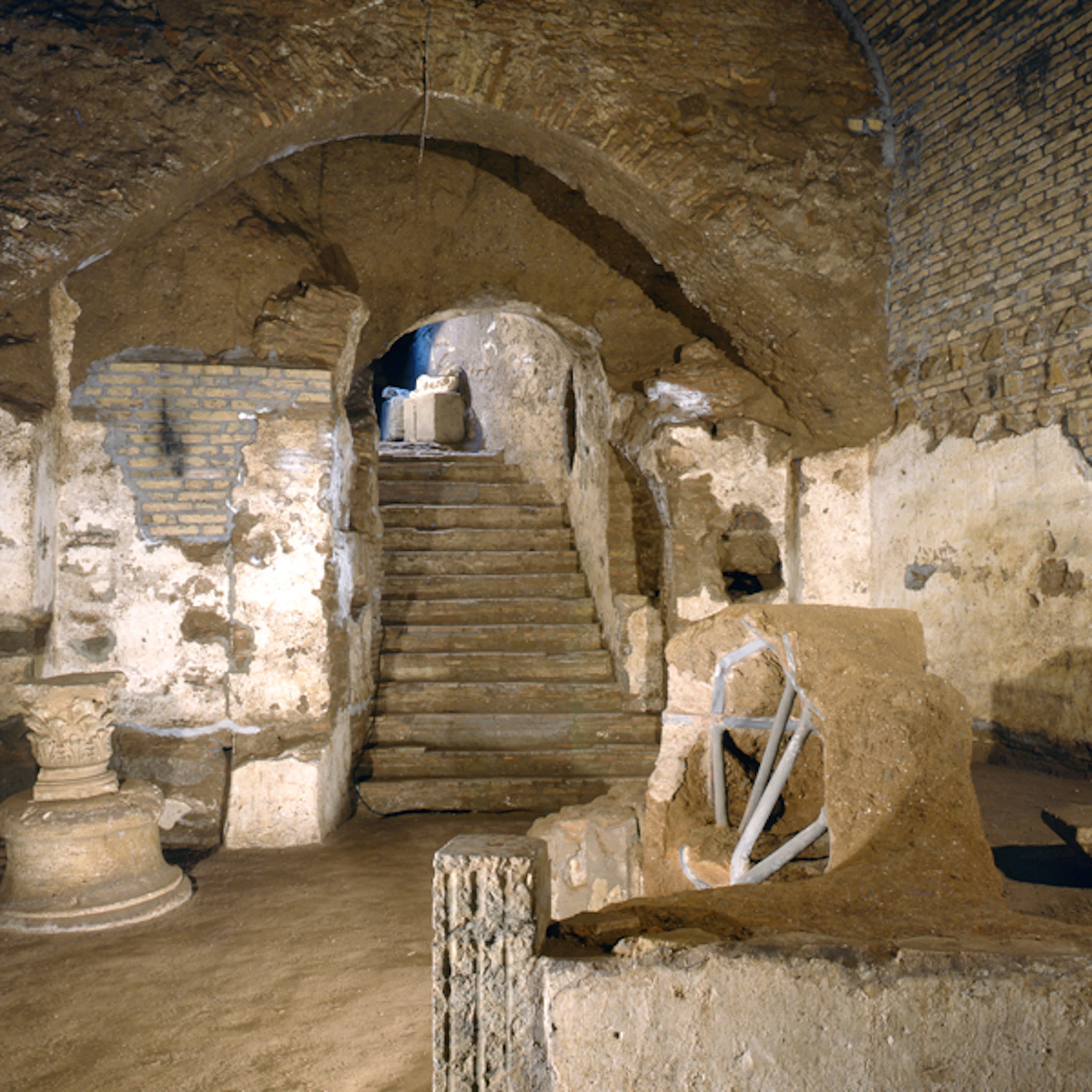 Ancient underground space with stone stairs, archways, and weathered walls. Various stone relics and artifacts are visible.